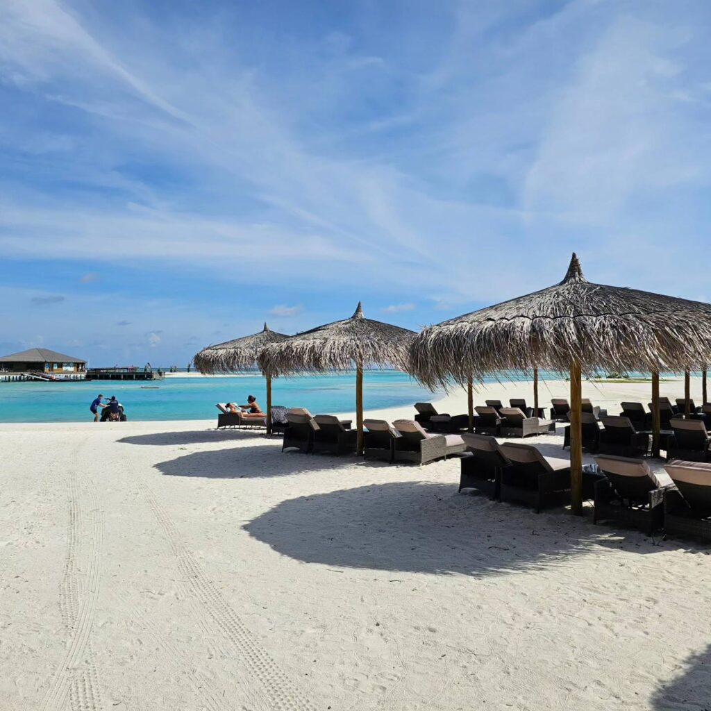 Foișoare cu acoperișuri din paie pe o plajă albă.