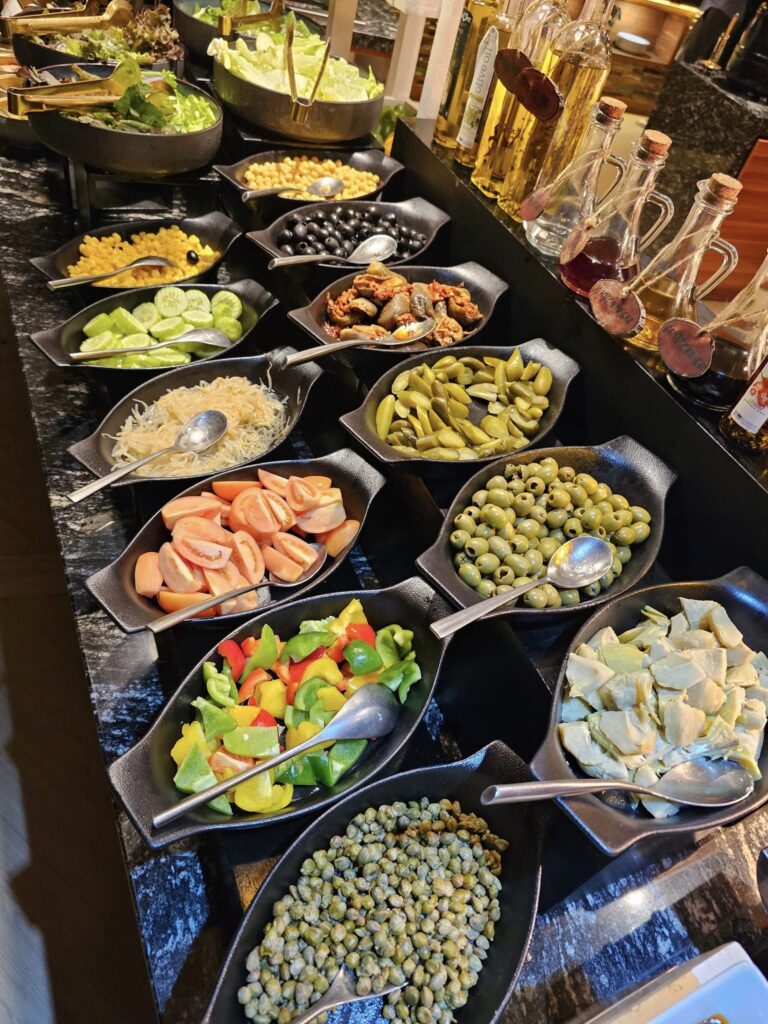 Boluri cu salate și legume aranjate pe un bufet.