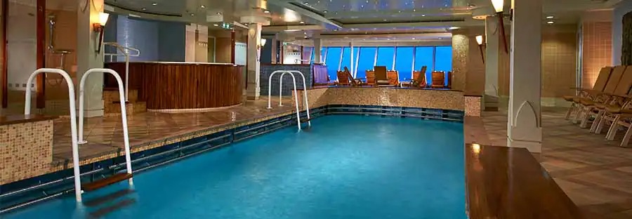 Piscină interioară cu scări metalice și șezlonguri.