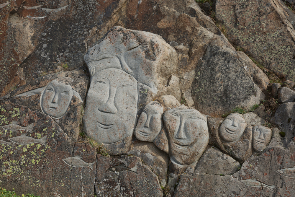 Chipuri stilizate sculptate într-un perete de piatră.