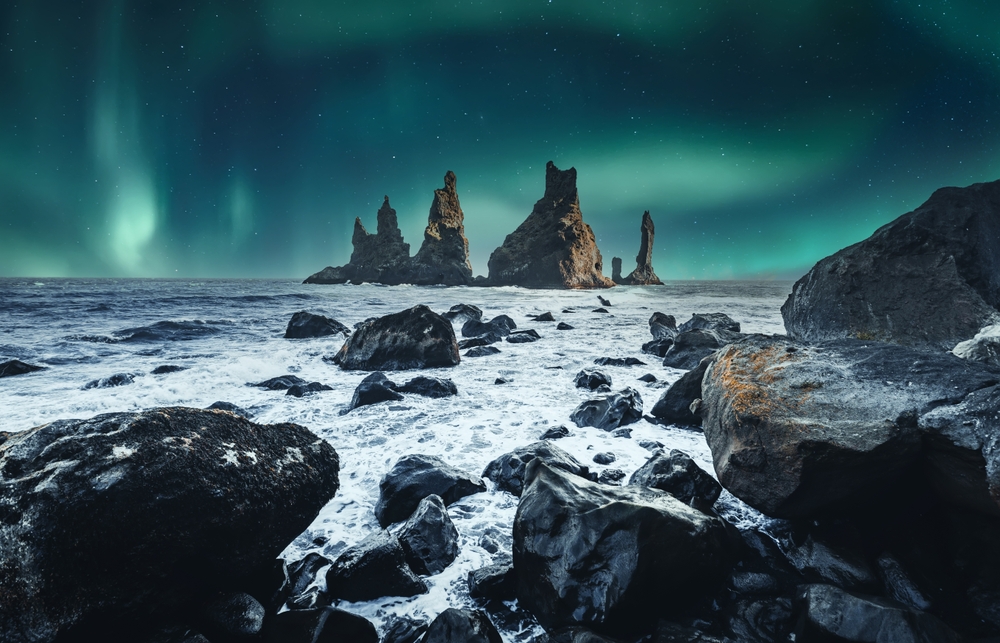 Auroră verde deasupra stâncilor și valurilor oceanului.