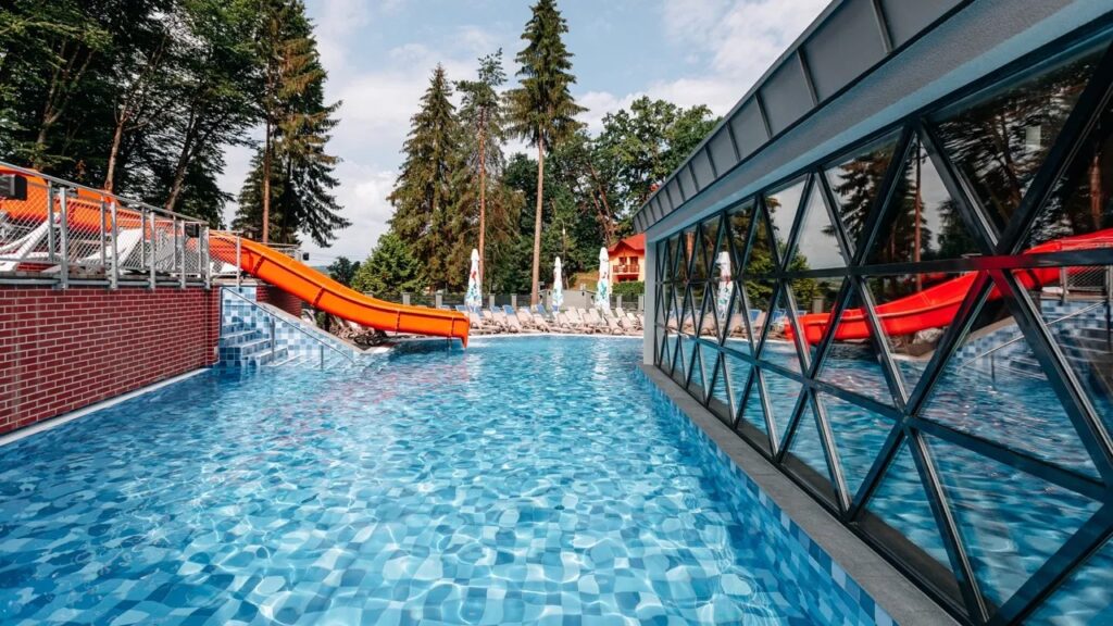 Piscină exterioară lângă un tobogan și o clădire cu geamuri.