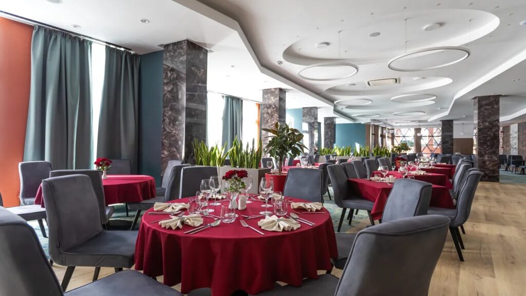 Sală de restaurant cu mese roșii și fotolii gri