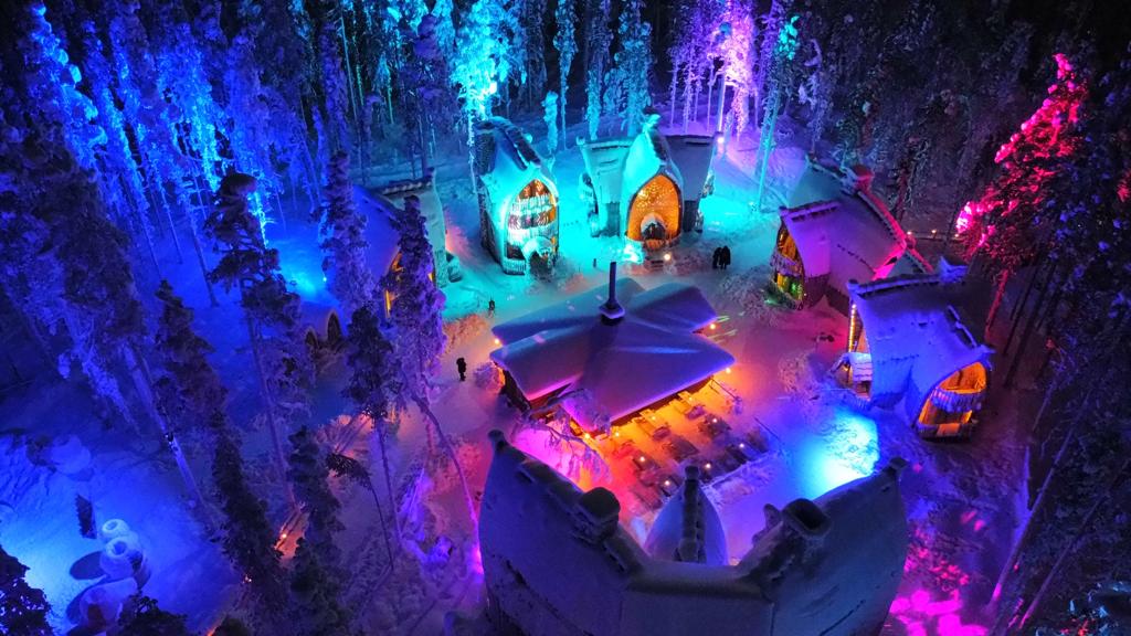 Construcții tematice iluminate albastru și violet, între arbori