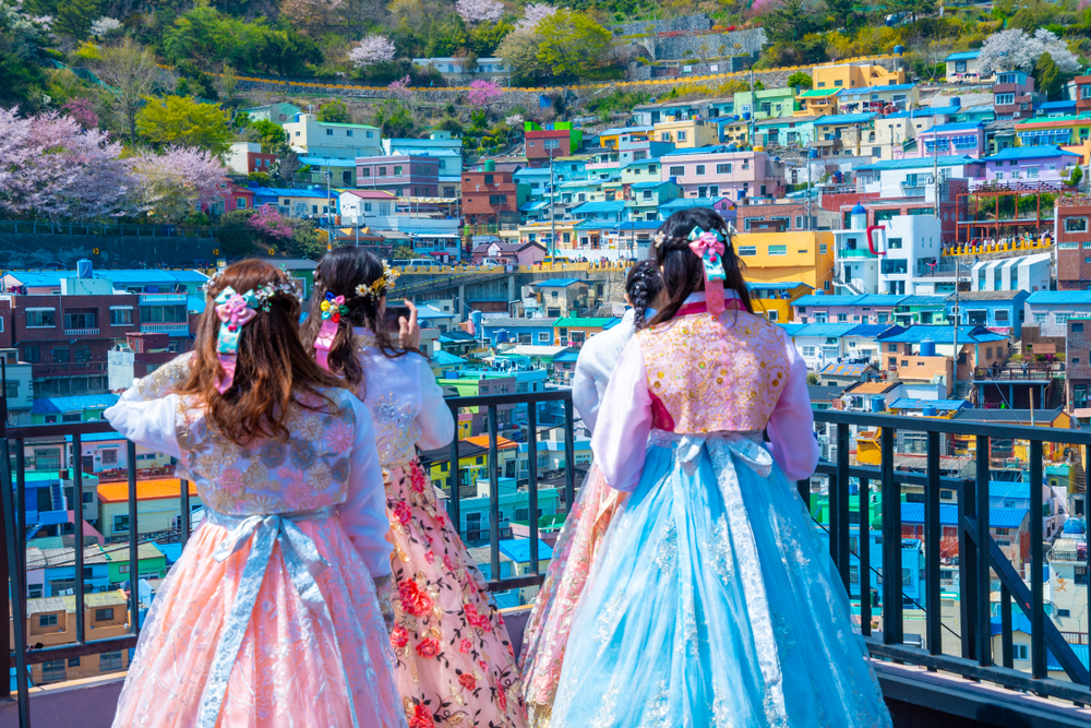 Două persoane în hanbok, privind casele de pe versant