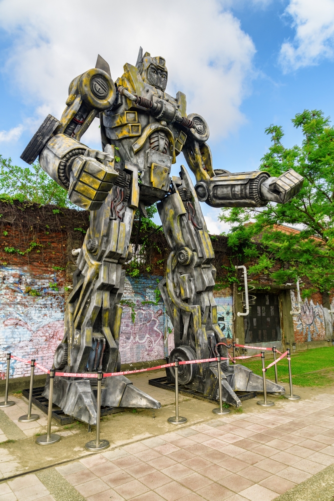 Sculptură mare de robot, expusă în aer liber lângă arbori.