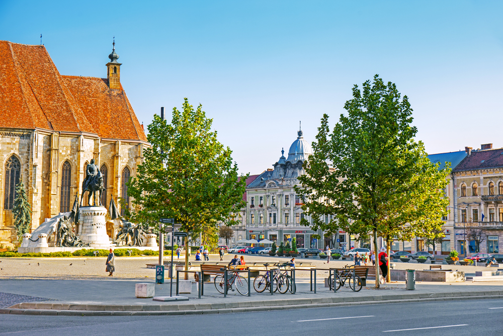 Piață urbană cu biserică, statuie și arbori în Cluj
