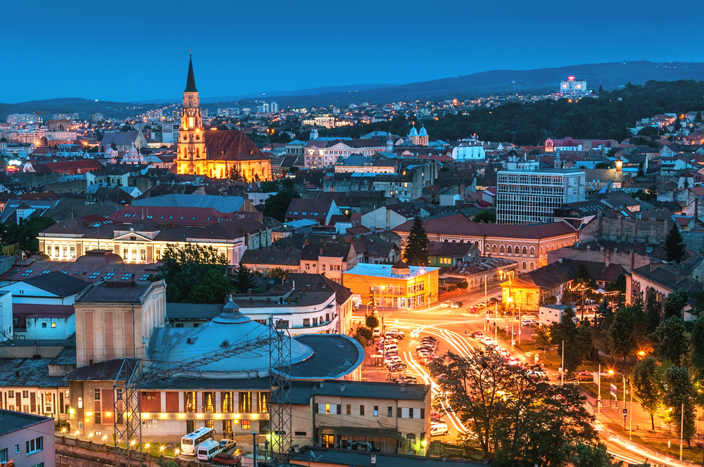 Panoramă urbană la înserat, cu biserică iluminată și piețe luminate.