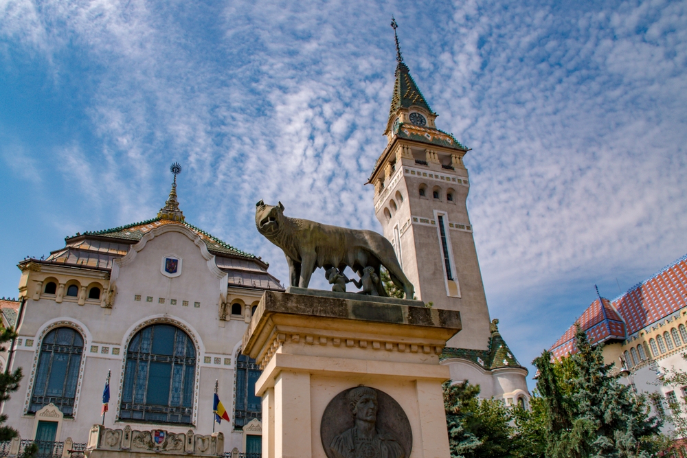 Clădire ornamentată cu turn înalt și acoperiș verde, sub cer albastru.