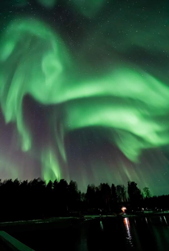 Auroră verde deasupra unei păduri, pe cer întunecat