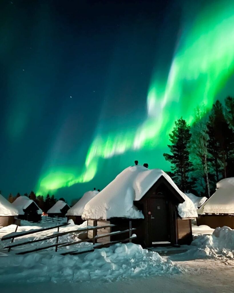 Auroră verde deasupra unei cabane acoperite de zăpadă