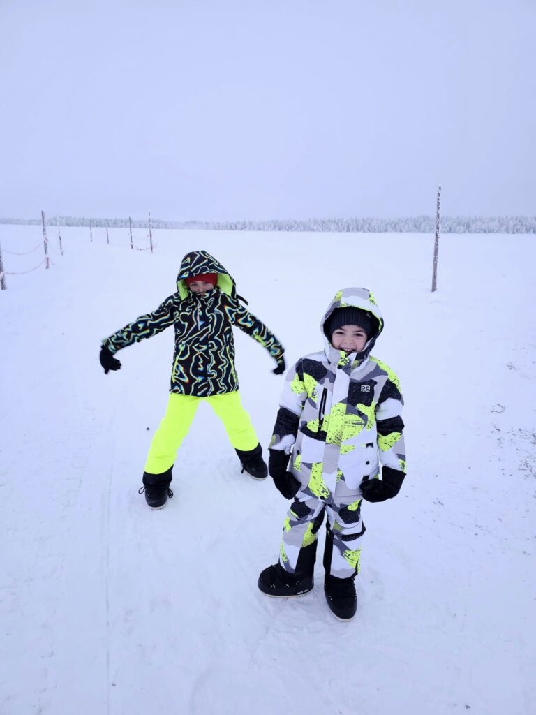Doi copii cu echipament de iarnă pe zăpadă