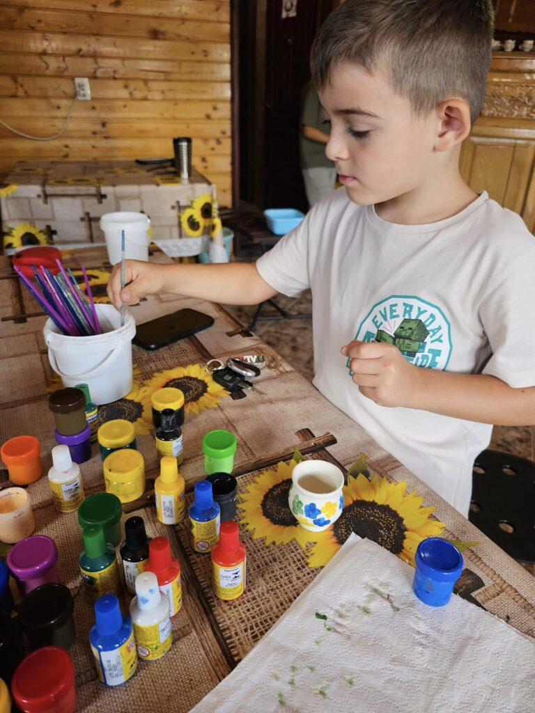 Copil pictând un obiect ceramic la o masă