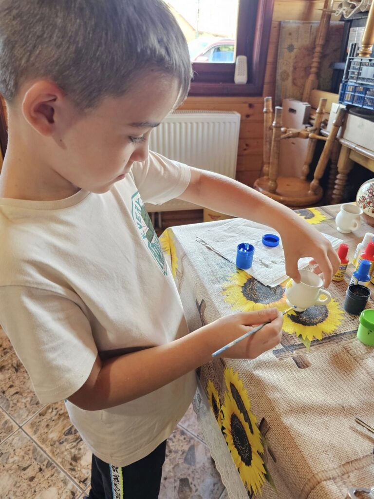 Copil pictând un obiect ceramic la masă