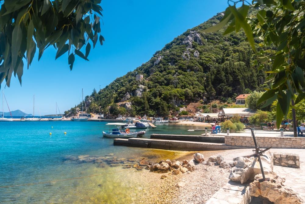 Bărci trase lângă o plajă pietroasă, sub un deal verde