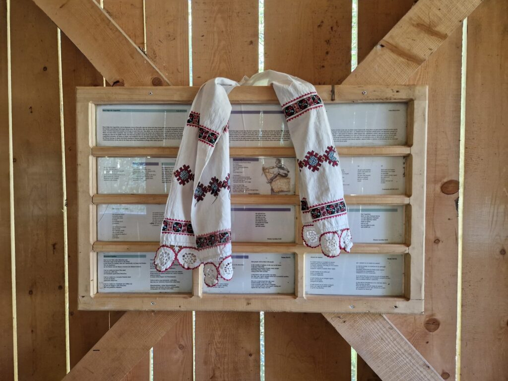 Cămașă brodată expusă peste panouri cu texte, într-o structură din lemn