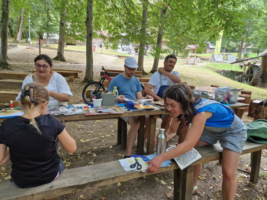 Participanți lucrând la mese lungi printre copacii unei păduri