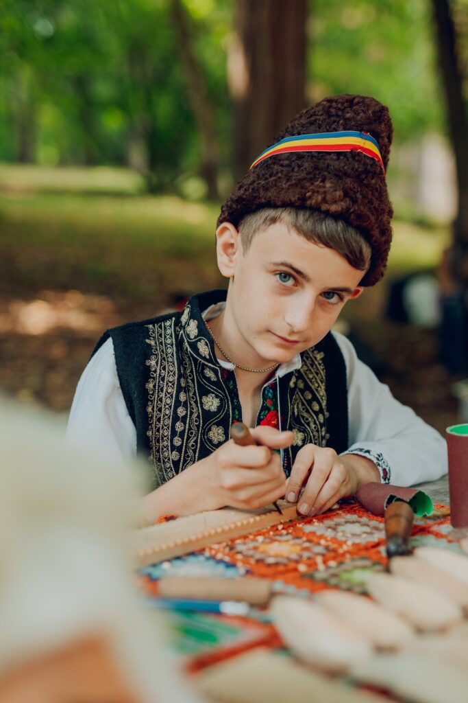 Copil cu căciulă și vestă brodată lucrând la masă
