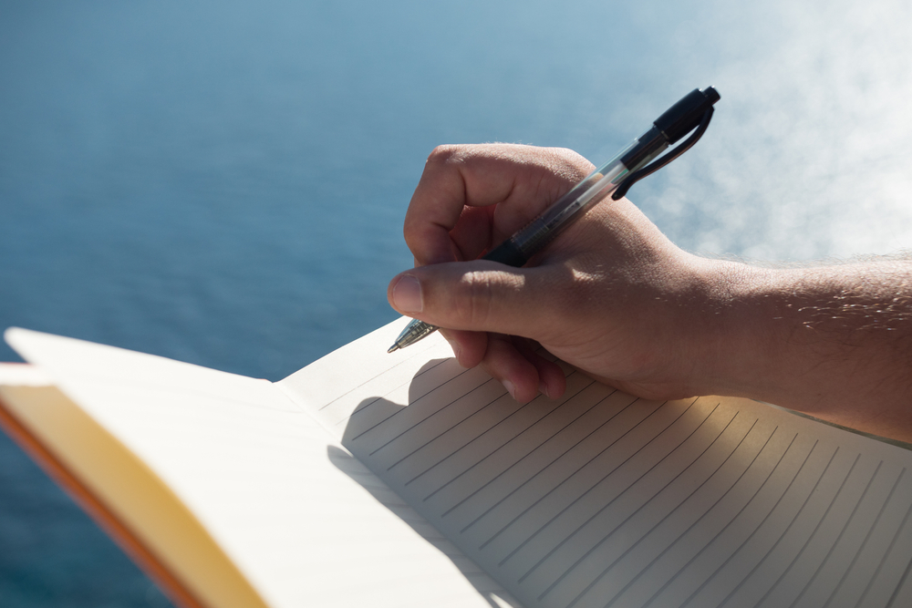 Mână scriind într-un caiet deschis lângă apă
