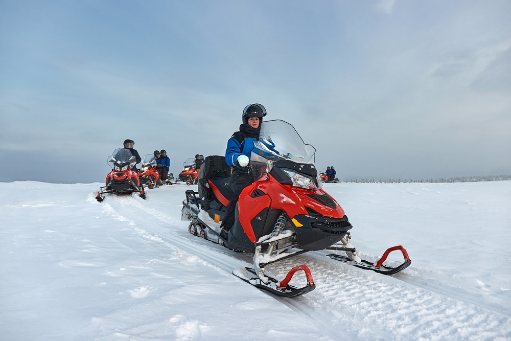 Persoane pe snowmobile, într-un peisaj alb