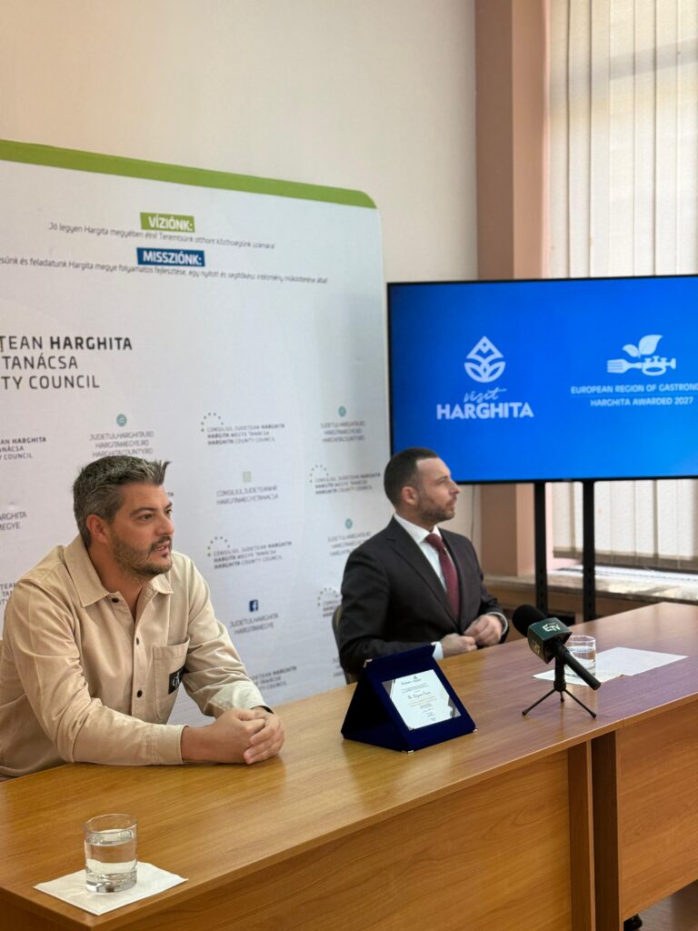 Doi bărbați la o masă, într-o sală de conferințe