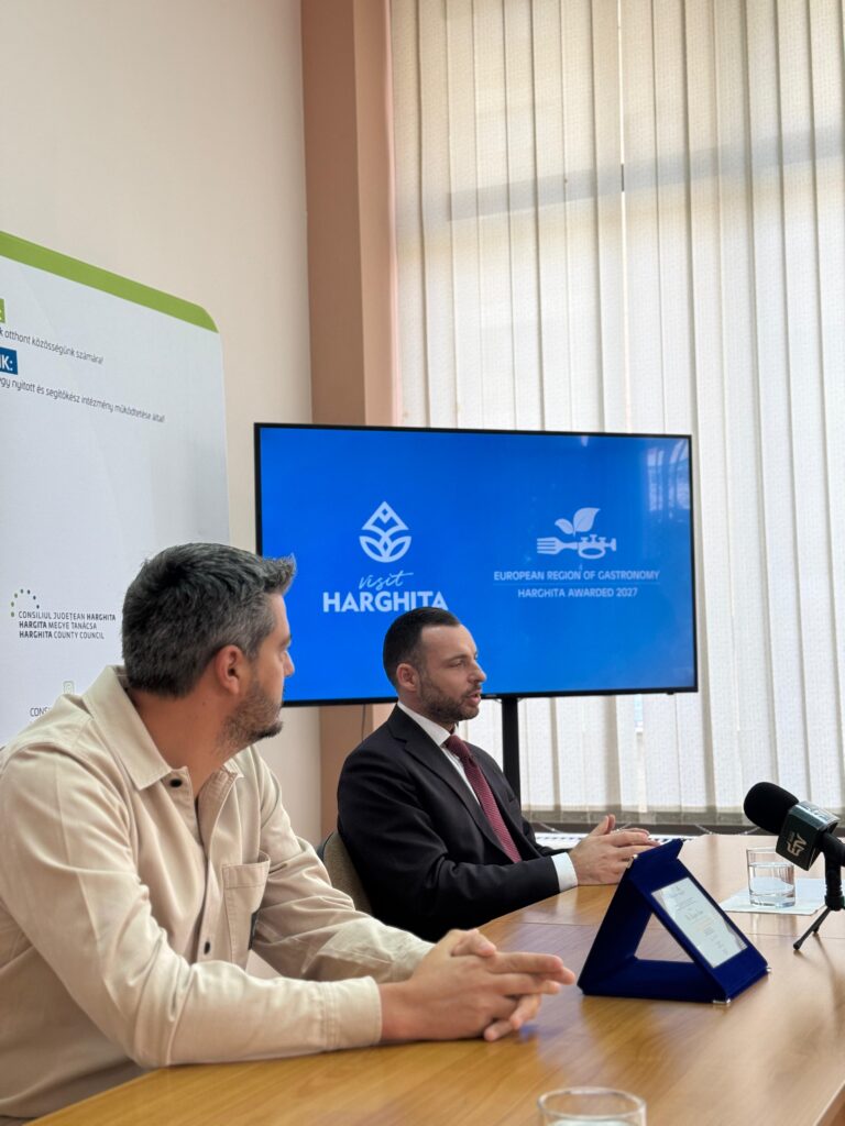 Doi participanți discutând la masă, într-o sală de conferințe