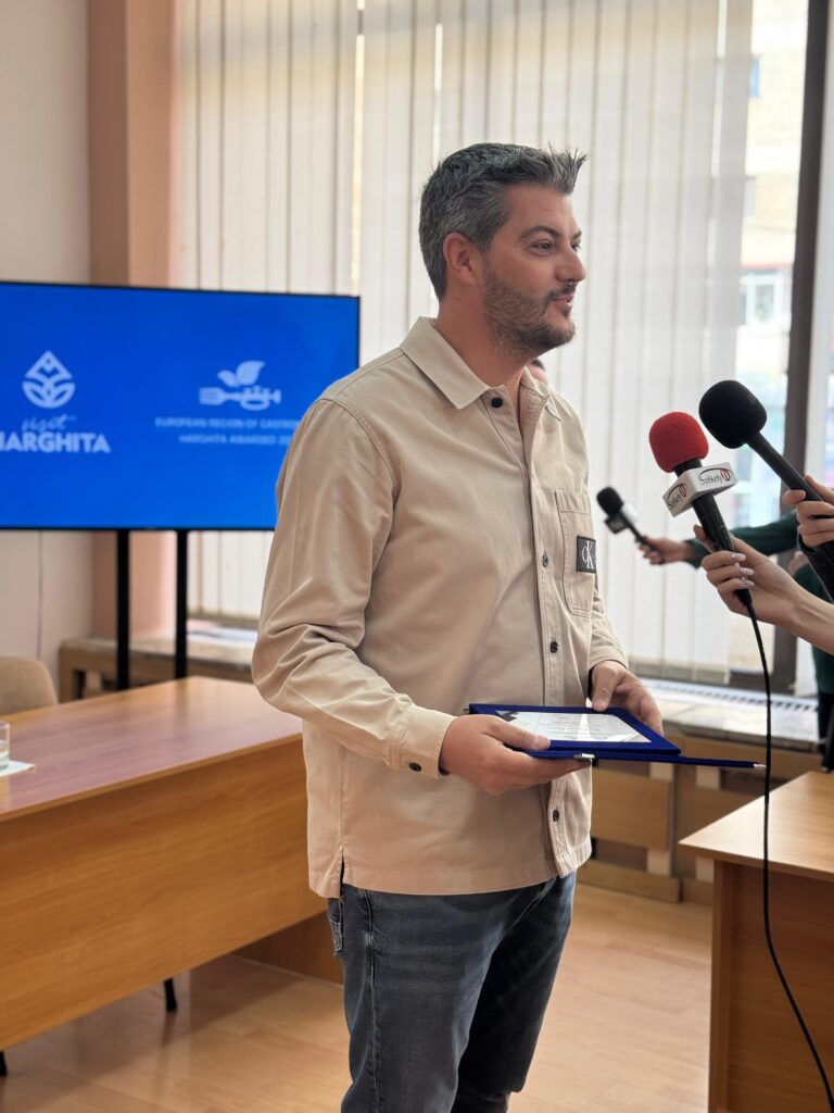 Bărbat vorbind la microfoane în fața unui ecran