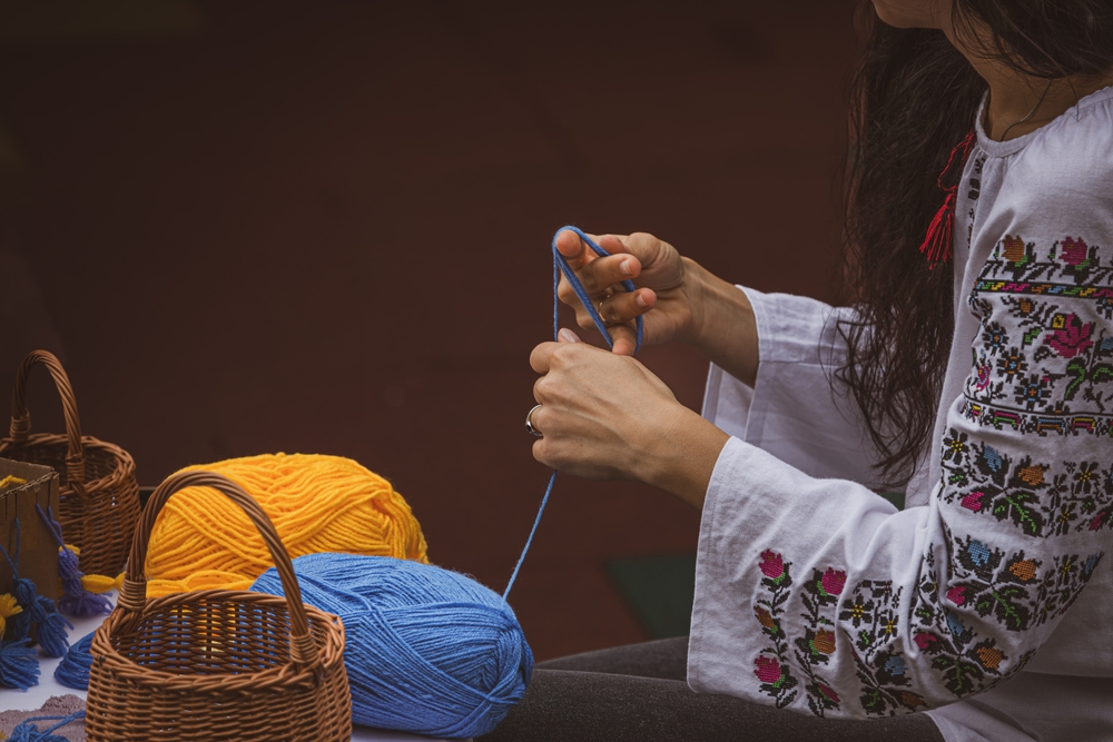 Persoană tricotând lângă ghemuri de lână colorată