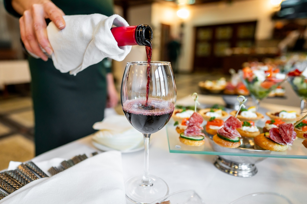 Vin turnat într-un pahar lângă farfurii cu preparate