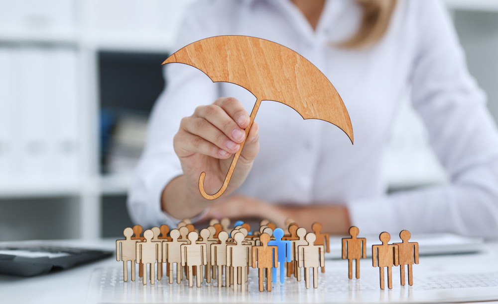 Mână cu umbrelă miniaturală deasupra unor figurine umane