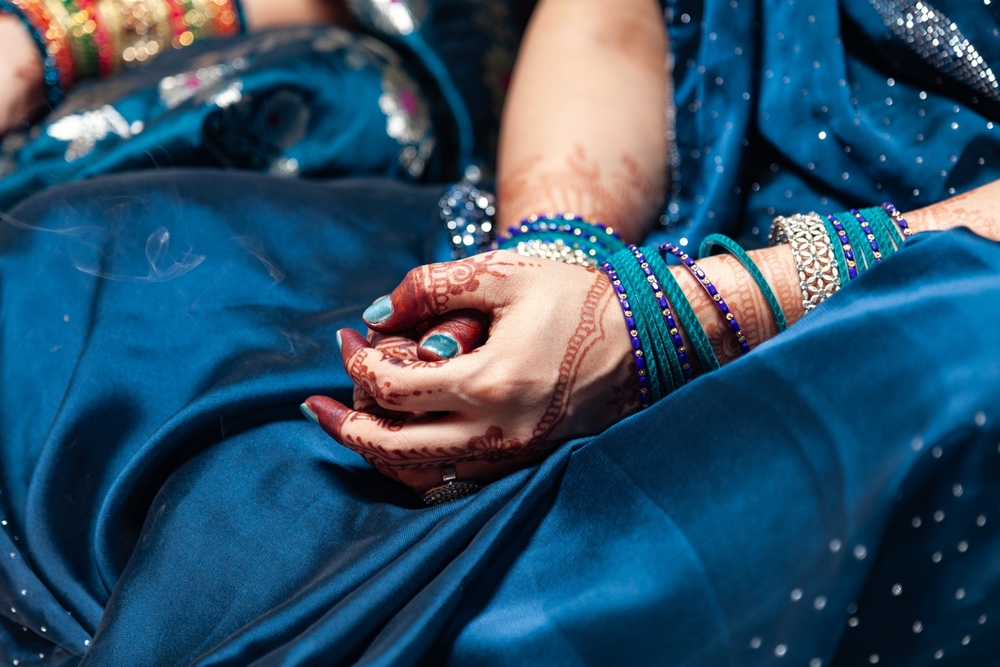 Mâini decorate cu henna și brățări, pe un sari albastru