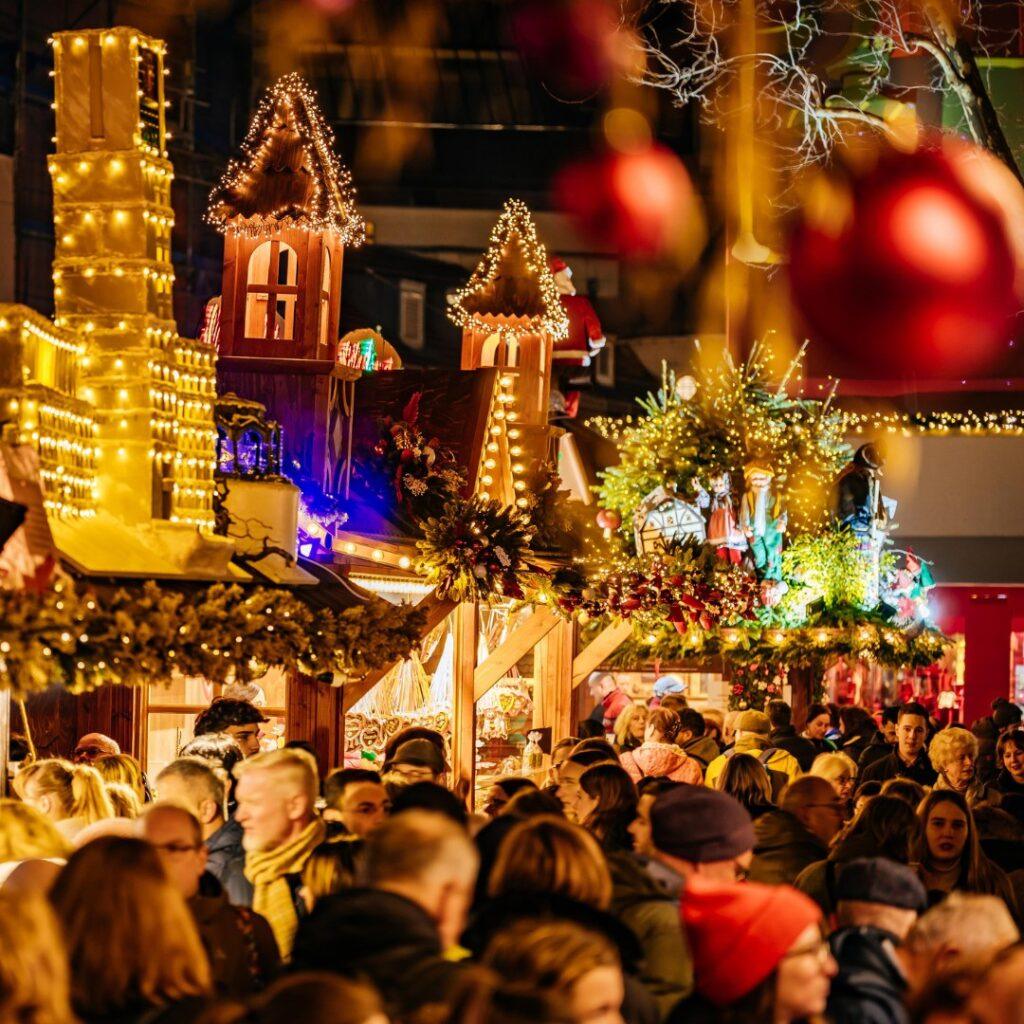 Târg de Crăciun iluminat, cu mulțime și globuri decorative