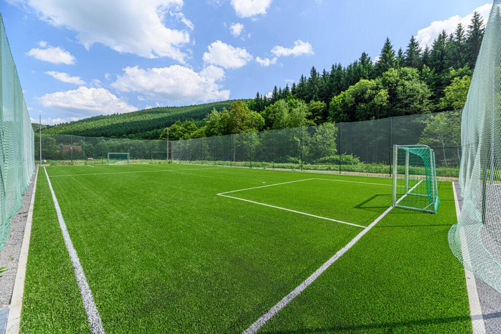 Teren de fotbal cu poartă, între dealuri împădurite