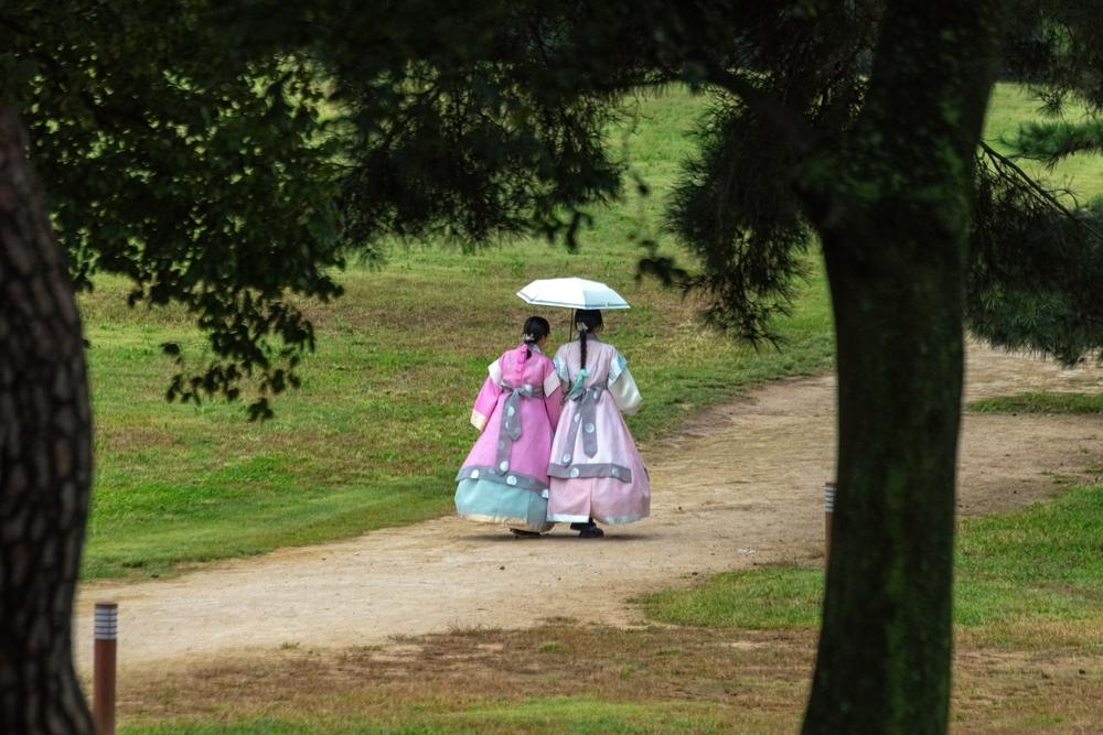 Două persoane în hanbok, plimbându-se printr-un parc