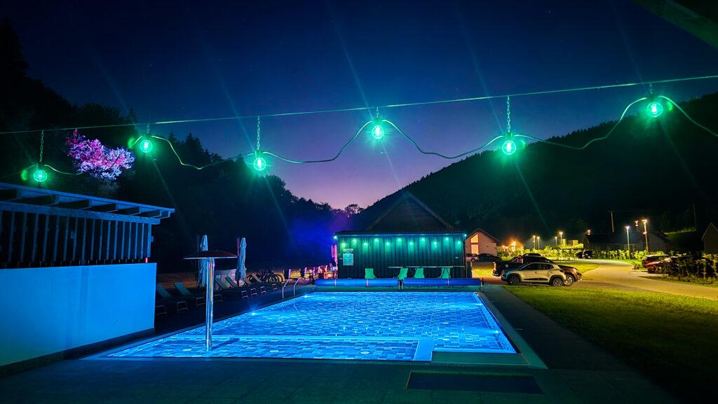 Piscină iluminată noaptea, cu ghirlande deasupra apei