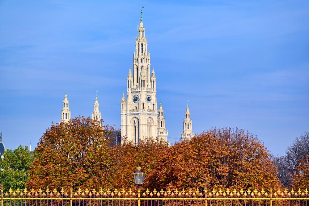 Clădire monumentală cu turn înalt, printre arbori de toamnă